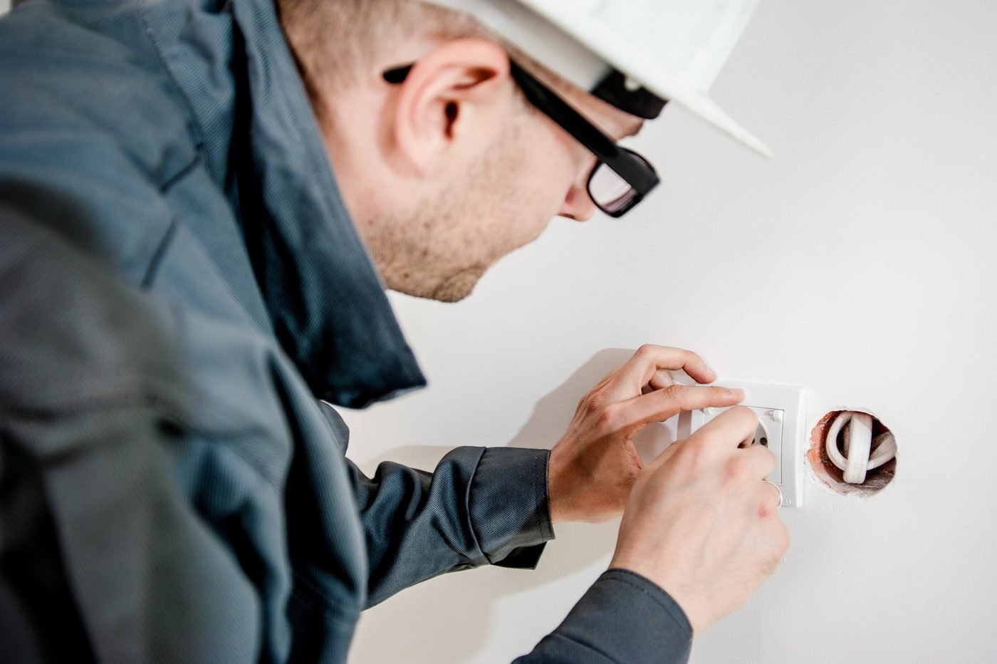 Elektrikas su apsauginiu šalmu montuoja elektros lizdą sienoje