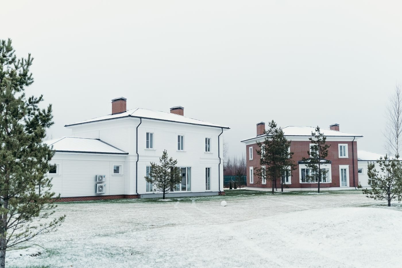 Baltas dviejų aukštų namas žiemą, ant sienos sumontuoti du šilumos siurblio lauko blokai