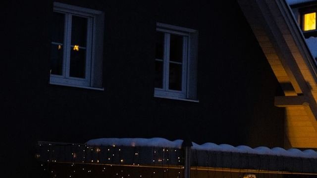 Apsnigtas gyvenamasis namas sutemus, languose dega šilta šviesa
