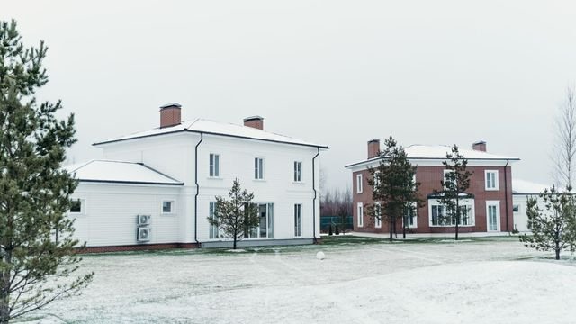 Baltas dviejų aukštų namas žiemą, ant sienos sumontuoti du šilumos siurblio lauko blokai